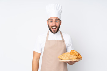 Male baker holding a table with several breads isolated on white background with surprise facial expression