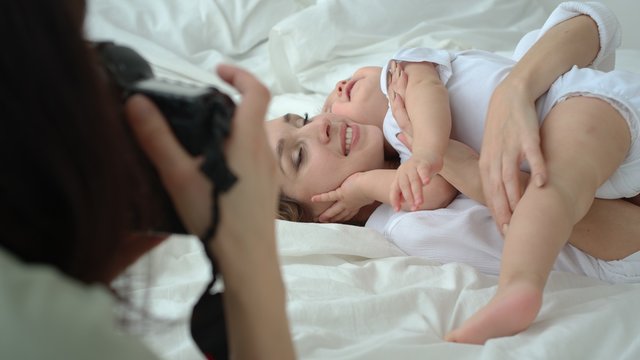 Young Mom Playing And Cuddling With Her Infant Baby On Bed While Photoshoot