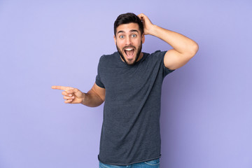 Fototapeta premium Caucasian handsome man surprised and pointing finger to the side over isolated purple background