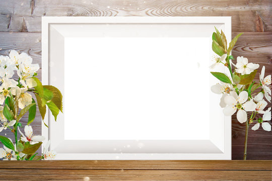 White photo frame on light wood background with cherry flowers