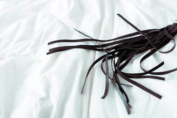 black leather flogging whip on white bedding