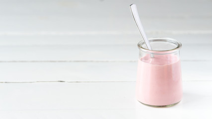 Pink strawberry, raspberry yogurt in a glass jar based on a right side on a white wooden background. 