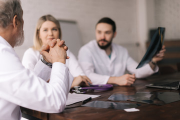 Team of three adult and young medical specialists discuss chest X-rays in the conference room of the hospital. Concept of team of doctors working together at the clinic. Concept of team medical work.