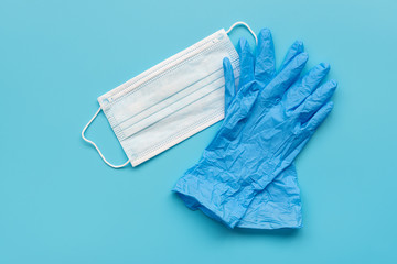 Pair of latex medical gloves and surgical ear-loop mask on blue background. Protection concept