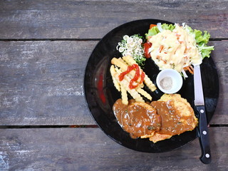 Handmade pork steak: Pork marinated with herbs, bake and serve with finely chopped herbs, french fries, vegetable salad, ground pepper and mellow sauce. Served in a black dish with steak knives