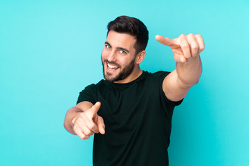 Caucasian handsome man isolated on blue background points finger at you while smiling