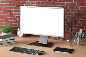Workspace with blank computer monitor white screen mock up on the wooden desk near red brick wall. 3d illustration