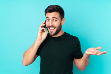 Caucasian handsome man isolated on blue background keeping a conversation with the mobile phone with someone