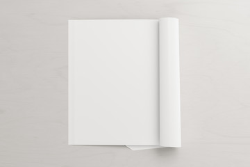 Blank vertical left magazine page. Workspace with folded magazine mock up on white desk. View above. 3d illustration