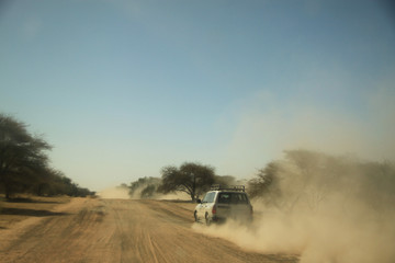 samochód terenowy mknący po szutrowej drodze afrykańskiej sawanny zostawiający za sobą chmurę kurzu
