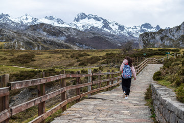 Fototapeta na wymiar young woman walking on a pathway to some beautiful snowed mountains on a really green landscape
