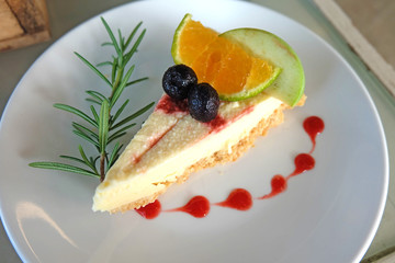 Cheesecake, cheese pie in the white plate and topping with cherry, orange and rosemary.