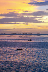 Small fishing boats with cargo ships and sunset sky