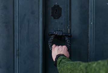Man holds hand door handle or knocker of ancient wooden door.