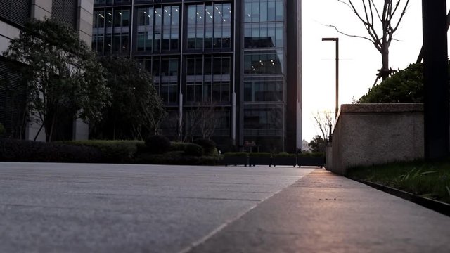 Hombre Joven patinando en skateboard en una plaza frente a un edificio durante el atardecer con los rayos del sol de frente a &eacute;l