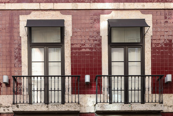 Two windows inserted into a concrete exterior pale red colored with azulejo wall of a building. 