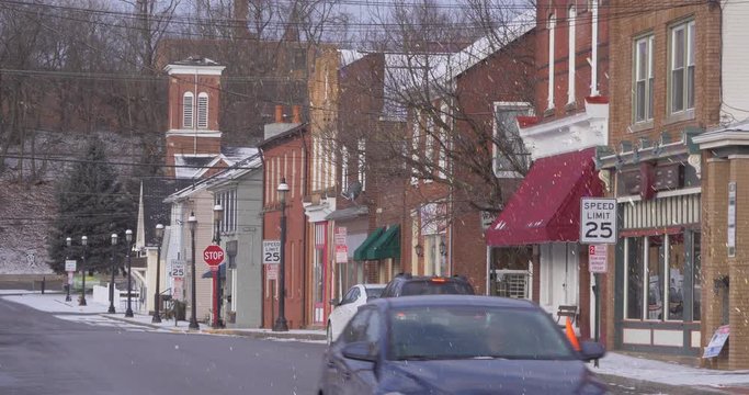 A daytime establishing shot of storefronts along a main street in a small town. Church steeple in distance. Non-snowing version available.  	