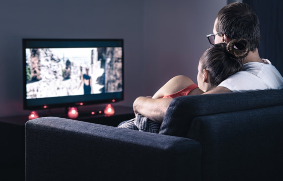 Couple watching movie or series. Online streaming and VOD service in tv screen. Film stream or television show. Cuddling during comfy and romantic candle light date at home. Man and woman relaxing.