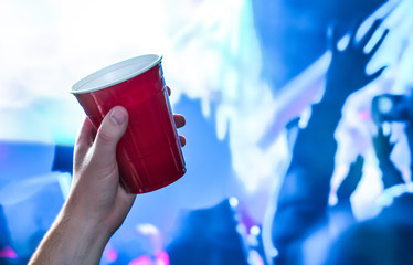 Red party cup in hand in night club, bar or college student event. Plastic beer mug. People having...