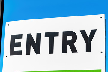 View of entry sign with black letters on white background and blue sky behind