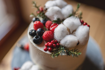 fashionable grey coloured winter theme cake with cotton flowers red berries raspsberries blueberries 