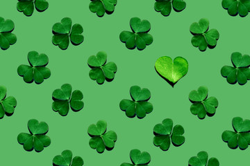 Pattern of shamrock leaves and one heart-shaped leaf on green background. St. Patrick's Day, selective focus.