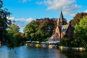 Fototapeta na wymiar Bruges, Belgium. August 2019. The lake and minnewater park are the most romantic place. The body of water on which the red brick castle and the large trees with green foliage are reflected.