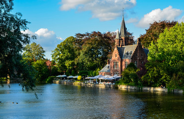 Bruges, Belgium. August 2019. The lake and minnewater park are the most romantic place. The body of water on which the red brick castle and the large trees with green foliage are reflected.