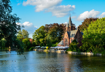 Fototapeta na wymiar Bruges, Belgium. August 2019. The lake and minnewater park are the most romantic place. The body of water on which the red brick castle and the large trees with green foliage are reflected.