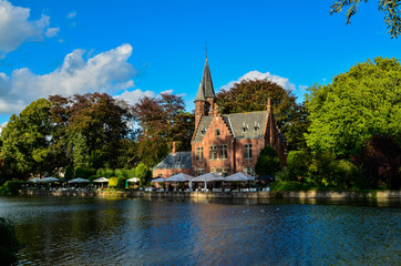 Obraz premium Bruges, Belgium. August 2019. The lake and minnewater park are the most romantic place. The body of water on which the red brick castle and the large trees with green foliage are reflected.