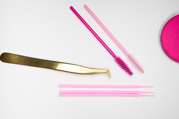  tools for eyelash extension, golden tweezers, pink brushes on a white background