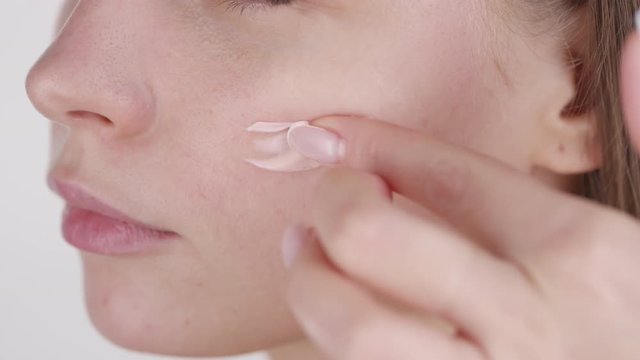 Extreme close up shot of beautiful woman putting dab of cream on face and smearing it with finger