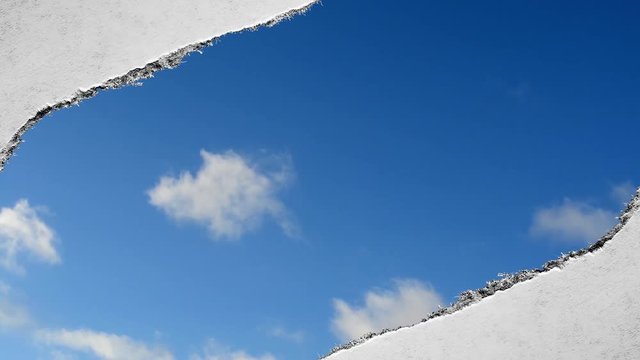 Creative time laps video of fast moving clouds in the blue sky that are visible through a hole with torn edges in old retro grunge vintage paper.