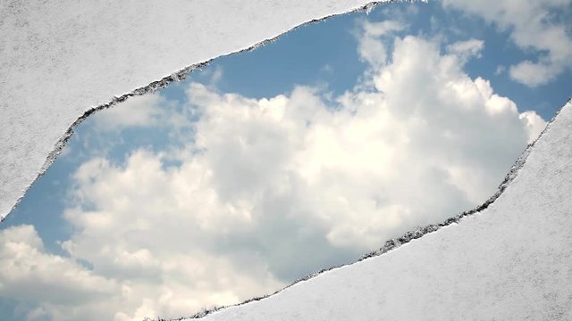 Creative time laps video of fast moving clouds in the blue sky that are visible through a hole with torn edges in old retro grunge vintage paper.