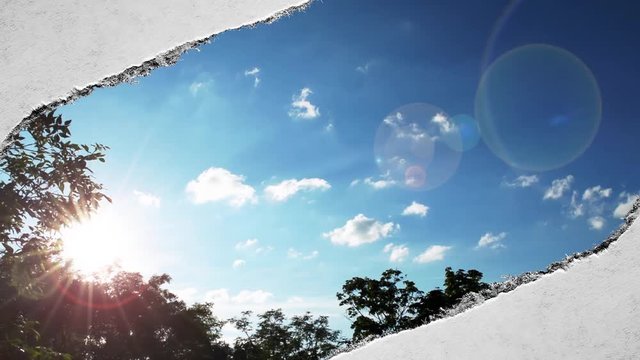 Creative time laps video of fast moving clouds in the blue sky at sunset witn sunflare that are visible through a hole with torn edges in old retro grunge vintage paper.