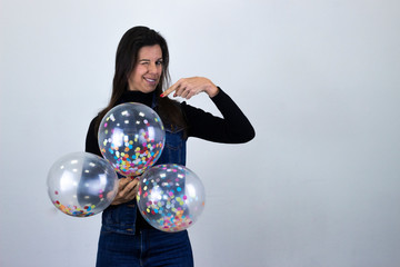 Portrait of thoughtful attractive middle age woman with party balloons thinks with finger on head, isolated on gray background studio shot, black sweater, denim jacket, jeans, dark air. Place for your