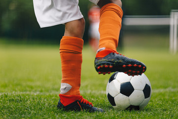 Soccer ball kick. Close up of legs and feet of football player in red socks and cleats running and dribbling with the ball. Soccer player running after the ball. Sports pitch and goal in background