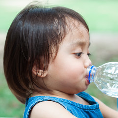 Asian toddler girl drinking water from the plastic water bottle.