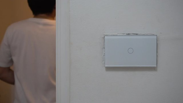 A man's hand is touching a fire switch in a modern home to turn on the light and urinate in the bathroom.