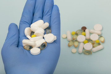 Different pills in hand in a medical glove on a blue background with pills