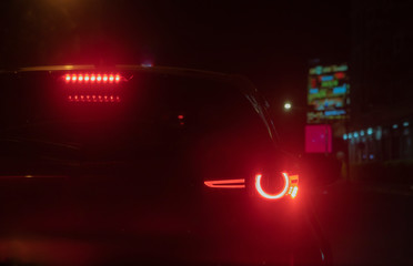 Red car rear lights of the black cars on the road are cutting the red traffic lights in heavy traffic.