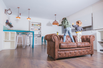 Back view of two kids dancing on the sofa at home.