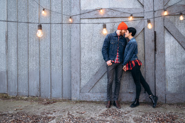 Young stylish couple is standing holding hands and gently cuddling on gray wall background