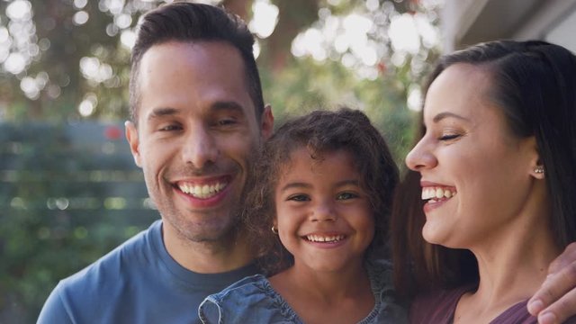 Portrait Of Smiling Hispanic Family With Daughter Laughing In Garden At Home