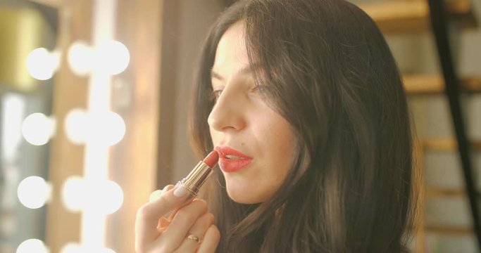 Beautiful girl paints lips with red lipstick close-up