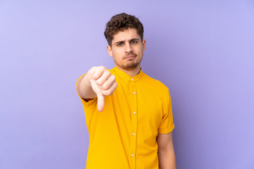 Caucasian man isolated on purple background showing thumb down with negative expression