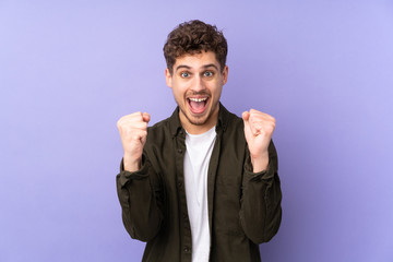 Caucasian man isolated on purple background celebrating a victory in winner position