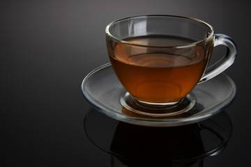 Glass cup of tea on a glass saucer with reflection, with a gradient of black and gray background. Concept, healthy and stylish lifestyle.