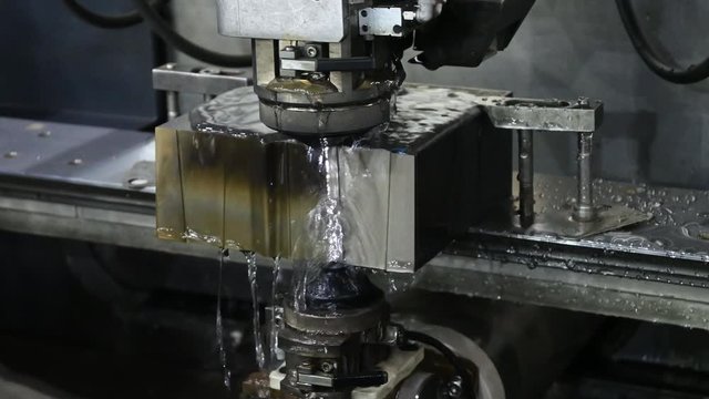 The operation of wire EDM machine cutting the die parts with coolant fluid. The hi-technology metal working process by wire cut machine control by CNC porgram.