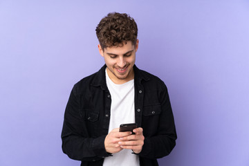 Caucasian man isolated on purple background sending a message with the mobile